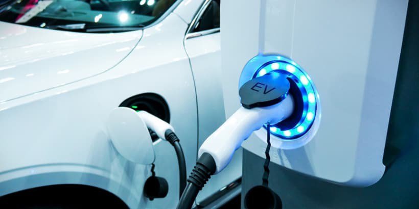 白い電気自動車が充電ステーションに接続されており、青く輝くEVプラグを見せています。