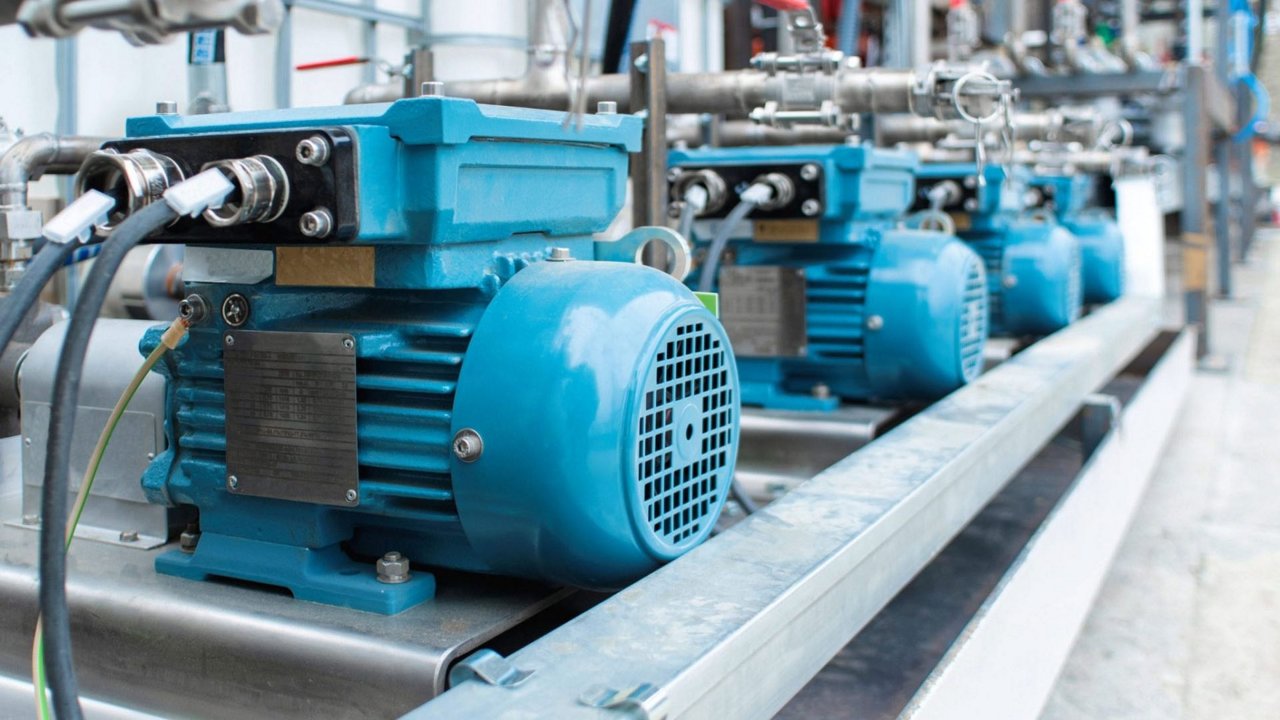 A row of blue industrial electric motors installed in a factory setting. 