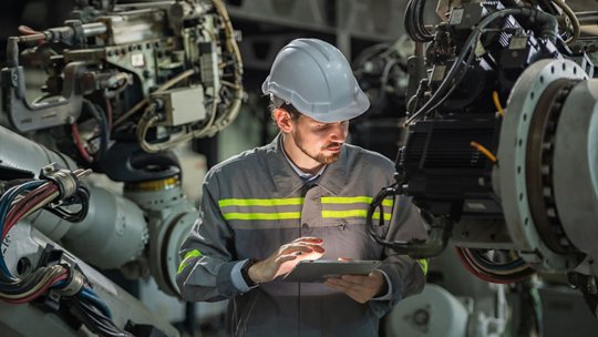 Male automation engineer in uniform helmet safety inspection check control heavy machine robot arm system in industrial factory. technician worker check for repair factory machine