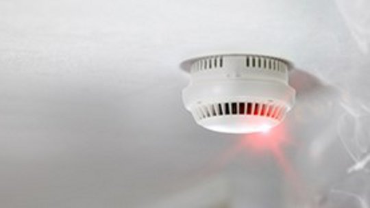 Image of a smoke detector with red light and smoke in the air