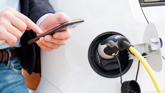 一名男子在为电动车充电时使用手机的照片