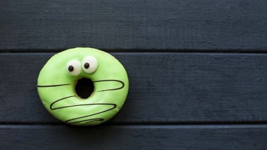 A vibrant green donut with a whimsical design featuring googly eyes and a surprised expression. 