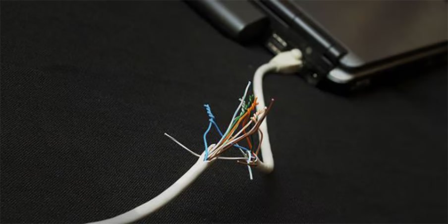 暗い表面上にラップトップの近くで、内部の配線が露出した損傷したネットワークケーブル。