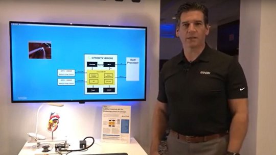 Man presenting a medical technology diagram, including a heart model, and a system architecture on a screen.