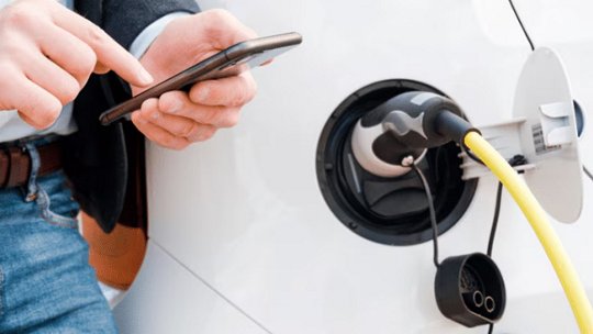 男性が電気自動車を充電しながらスマートフォンを操作している。