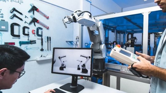 Ein Roboterarm wird in einem modernen industriellen Umfeld präsentiert, während ein Techniker in der Nähe ein Steuergerät bedient.