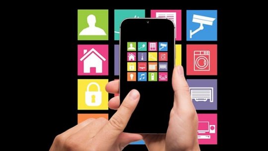スマートフォンを持つ手のクローズアップ。画面にはカラフルなホームオートメーションアイコンが表示されています。