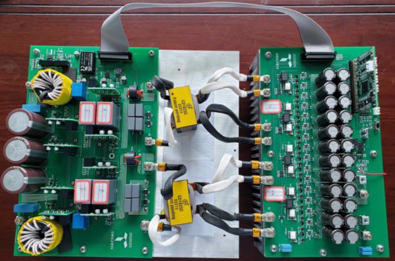 Two green electronic circuit boards are displayed on a wooden surface, featuring capacitors, transformers, and wiring connections.
