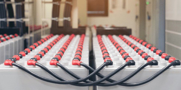 A large array of industrial batteries connected with black and red cables is displayed in a clean, indoor facility. 