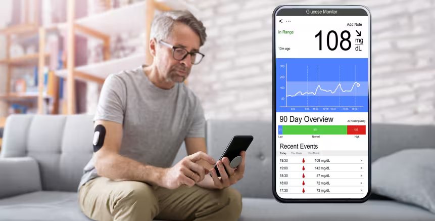 A man is seated on a couch in a modern living room, using a smartphone to check his glucose levels via a monitoring app.