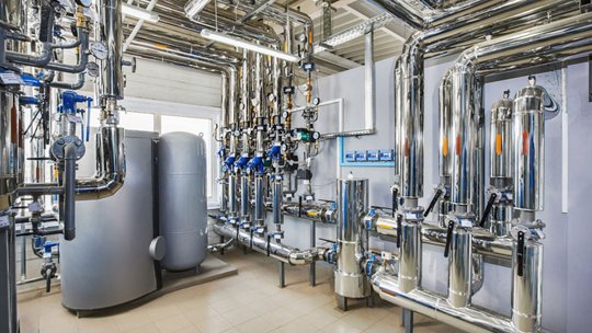 The Interior of an industrial boiler house with a multitude of pipes, barrels and sensors