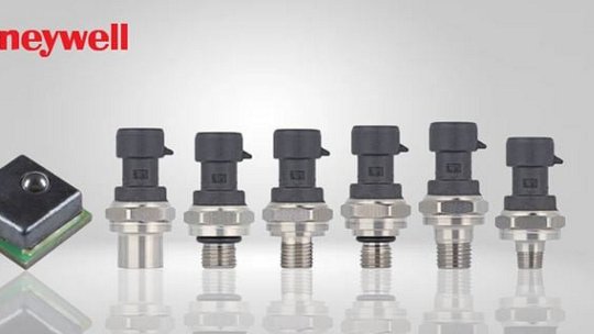 A lineup of Honeywell pressure sensors displayed against a neutral gray background. The image features six cylindrical sensors with metallic bases and black connectors, alongside a square sensor module. 