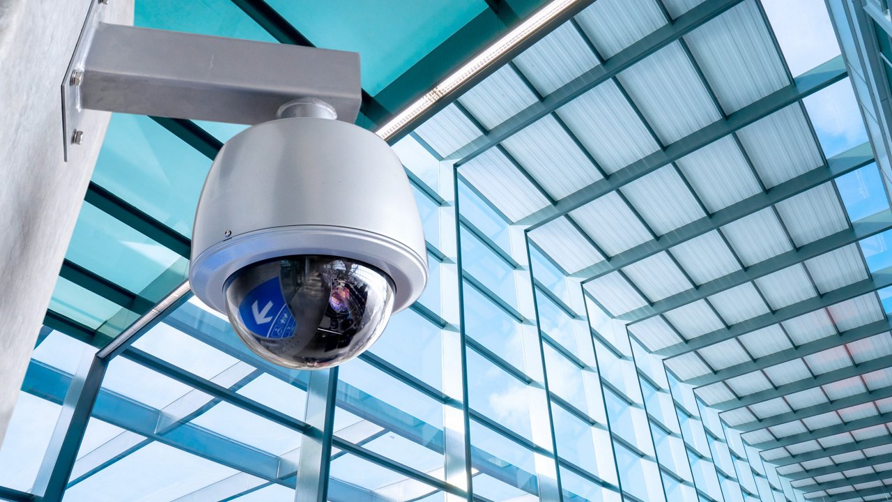 A sleek dome-shaped security camera mounted on a wall in a contemporary glass building