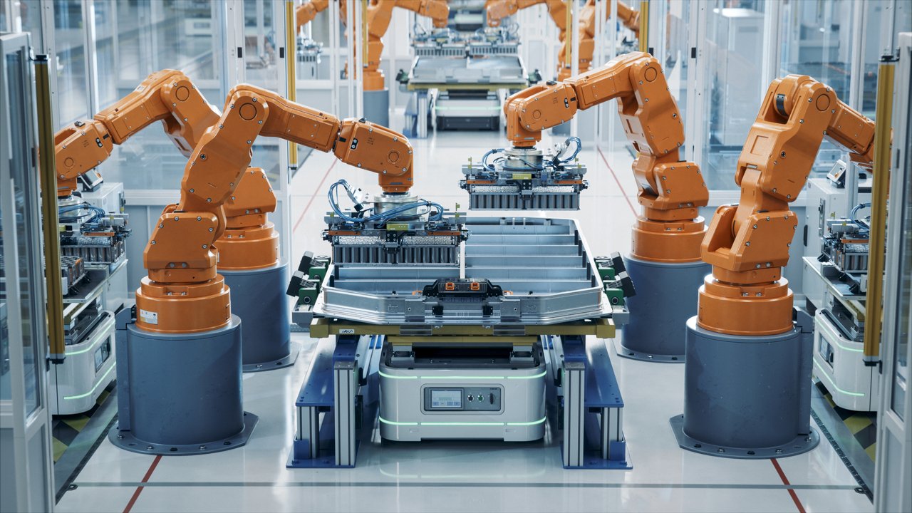 A group of orange robotic arms operates in a high-tech manufacturing facility, assembling components on a production line