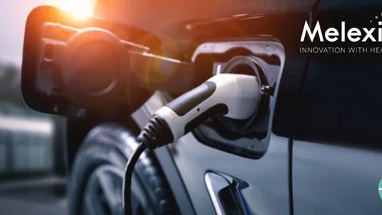 Ein Elektrofahrzeug wird beim Laden gezeigt, mit einer Nahaufnahme des Ladeanschlusses und des Kabels. Die Szene scheint sich im Freien bei Tageslicht abzuspielen, mit einem warmen Sonnenlichtschein. Das Melexis-Logo und der Slogan „Innovation mit Herz“ sind deutlich in der oberen rechten Ecke sichtbar.