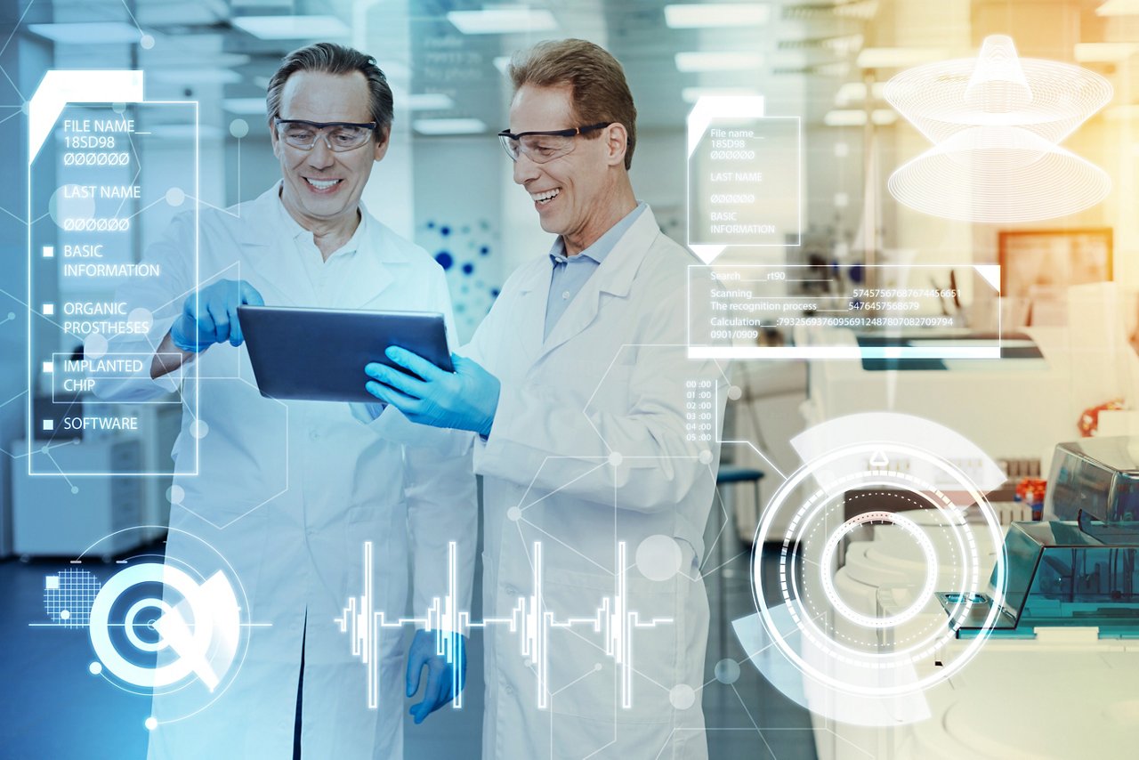 Two scientists in white lab coats are examining data on a tablet in a modern laboratory setting