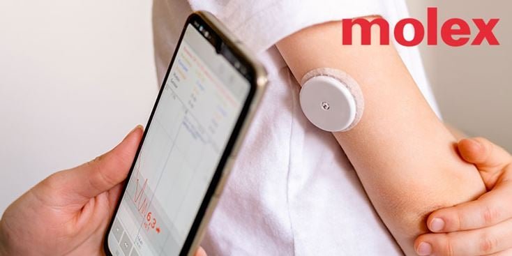 A wearable medical sensor is attached to a person's arm, paired with a smartphone displaying health data. The Molex logo is clearly visible in the image. The phone screen shows a graph and numeric data, including '6.3'. The setting suggests a health monitoring activity.