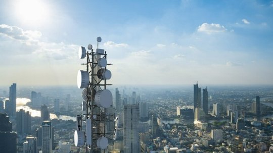 A telecommunication tower equipped with multiple antennas stands prominently against a sprawling cityscape. 