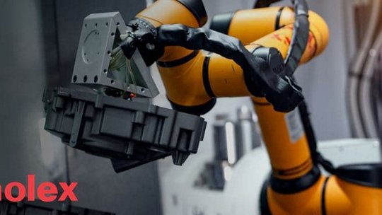 A yellow robotic arm is shown gripping a mechanical component in an industrial setting. 