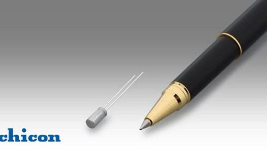 Un pequeño condensador Nichicon se muestra al lado de una pluma fuente negra con detalles dorados.