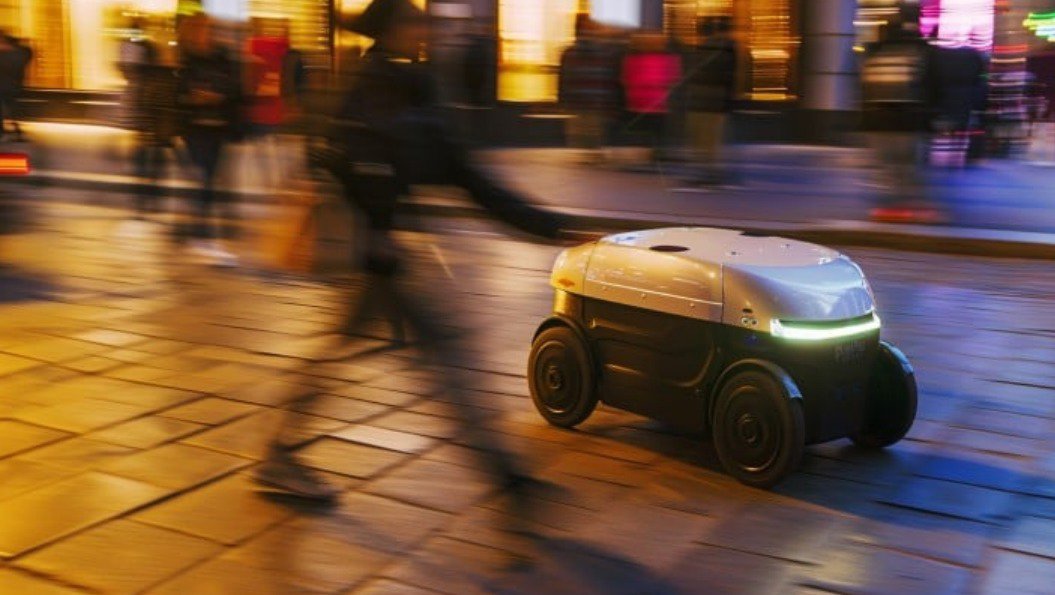 A compact autonomous delivery robot navigates a busy city street at night