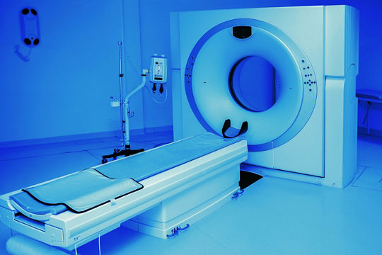 A contemporary CT scanner positioned in a medical examination room. The setting features a clean, sterile environment with blue lighting that emphasizes the equipment's design.
