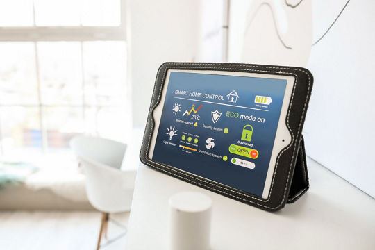 A tablet displaying smart home control features is placed on a white surface in a bright, modern room.