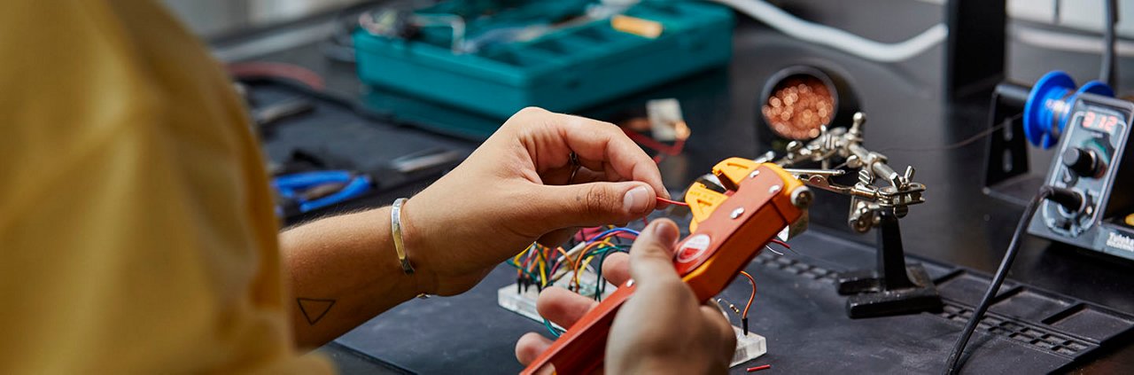 Close-up of hands assembling electronic components using a crimping tool in a workshop setting. 