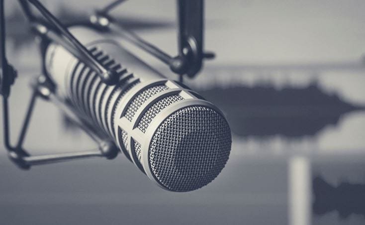 녹음실 환경에 설치된 금속 메시 디자인의 전문 마이크를 근접 촬영한 모습입니다. 배경에는 흐릿한 사운드 웨이브 비주얼이 보여져 있으며, 이는 오디오 제작을 강조합니다. 단색 팔레트는 세련되고 현대적인 미감을 연출합니다.