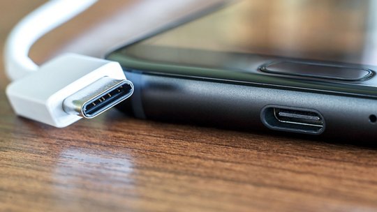 A detailed view of a USB-C cable positioned near a smartphone's charging port. The image highlights the sleek design of the cable and the device, set against a wooden surface.