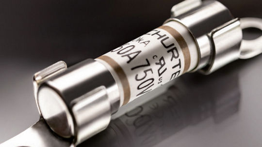 A detailed view of a cylindrical industrial fuse with metallic ends and visible labeling.