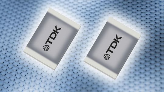 Two TDK electronic components are displayed on a textured, metallic surface.