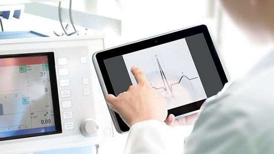 A medical professional interacts with a tablet displaying heart rate data in a clinical setting