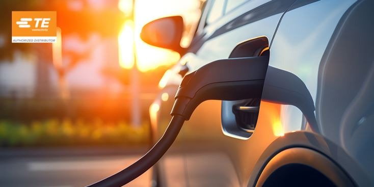 夕暮れ時、充電ステーションで電気自動車が接続されているクローズアップの様子。暖かい照明と現代的な車のデザインが特徴的なシーンです。画像の左上には「TE」ロゴが見え、ブランド要素が加わっています。