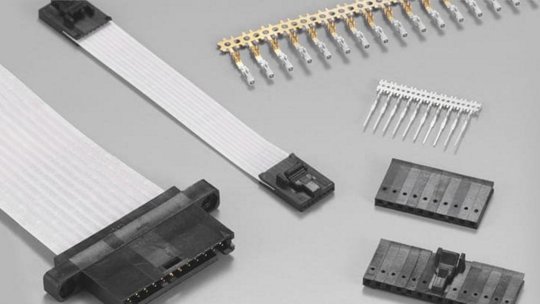 A flat ribbon cable with black plastic connectors is displayed alongside gold-plated pins and additional connector components