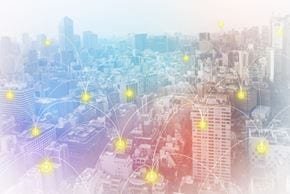 高層ビルと広がるスカイラインが広がる都市の景観に、輝くデジタルネットワークノードが重ねられています。この画像は、接続性と現代技術の感覚を伝えています。色彩は、青、赤、白の柔らかなグラデーションを含み、未来的な雰囲気を生み出しています。