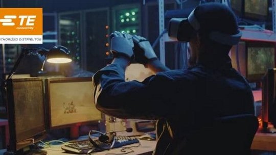 Un hombre con un casco de realidad virtual y guantes interactúa con un entorno digital en un espacio de trabajo tecnológico tenuemente iluminado.