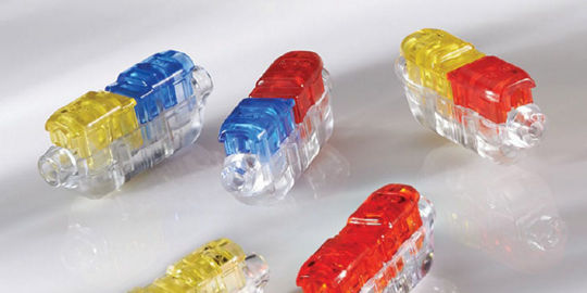 Five transparent electrical connectors with vibrant red, yellow, and blue accents are arranged on a glossy white surface. 