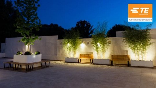 A contemporary outdoor patio featuring minimalist benches and planters illuminated by warm evening lights.