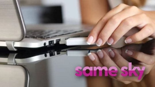 銀色のスリムなノートパソコンのポートにUSBデバイスを差し込む手のクローズアップ。
