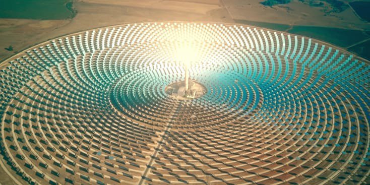 Una gran planta de energía solar con una torre radiante central rodeada de arreglos concéntricos de espejos. El escenario parece ser un remoto paisaje desértico bajo cielos despejados. La imagen destaca la tecnología de energía renovable y la simetría geométrica de la instalación.