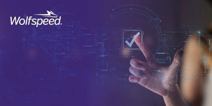 Un'interfaccia digitale futuristica con un segno di spunta luminoso è evidenziata su uno sfondo blu. Il logo di Wolfspeed è ben visibile nell'angolo in alto a sinistra. Una mano interagisce con l'interfaccia, suggerendo innovazione e tecnologia. La scena trasmette un'atmosfera moderna e ad alta tecnologia.