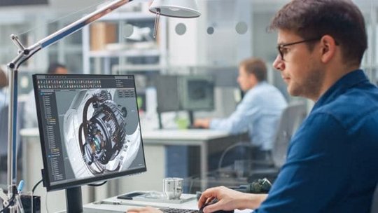 現代的なオフィス環境で、プロフェッショナルなエンジニアが机に座り、詳細な3D機械設計を表示しているコンピューターで作業をしています。