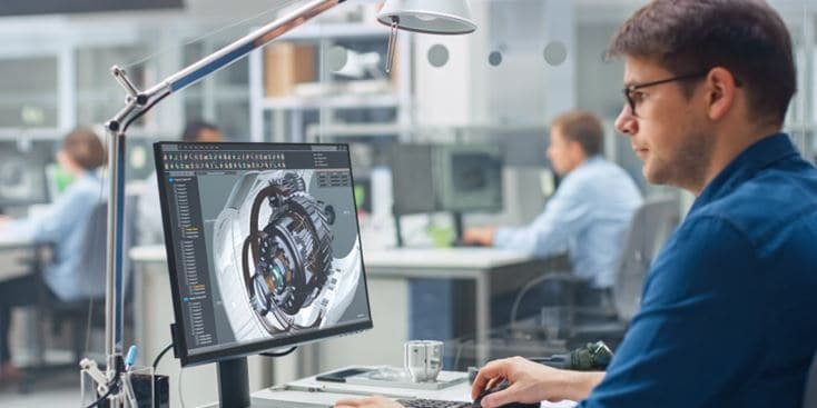 プロのエンジニアが、現代的なオフィス環境のデスクに座り、詳細な3D機械設計を表示しているコンピューターで作業しています。